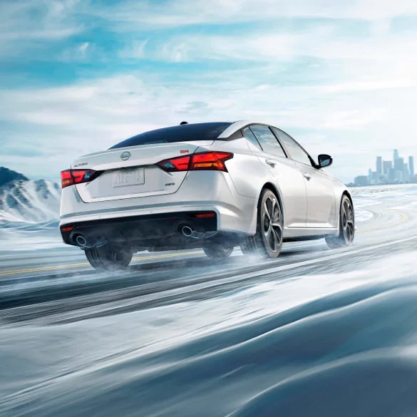 2027 Nissan Altima in white seen from behind driving in snowy landscape illustrating all-wheel drive at Dublin Nissan in Dublin GA